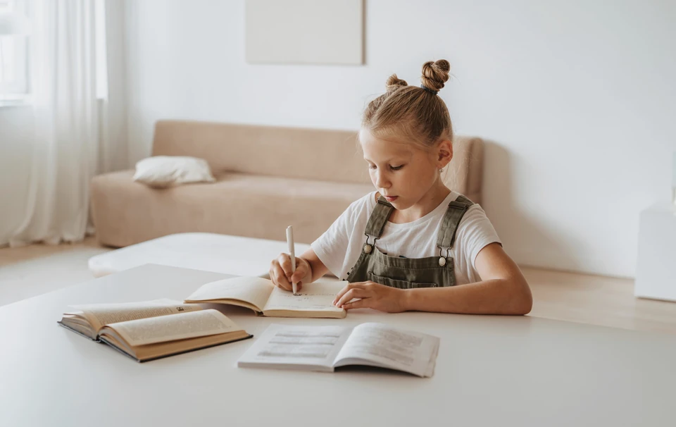 Basisschoolleerling schrijft aan tafel in een lichte kamer.