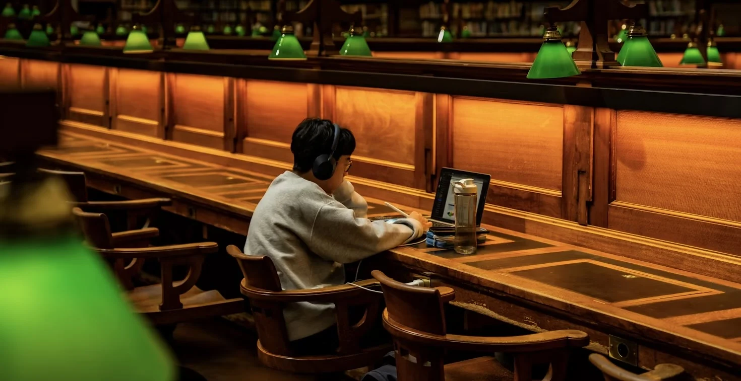 Leerling studeert geconcentreerd in een warme bibliotheekomgeving.
