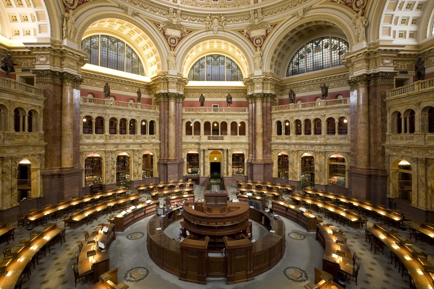 Monumentale bibliotheekzaal met ronde leestafels en galerijen als beeld voor instituut en kwaliteit.
