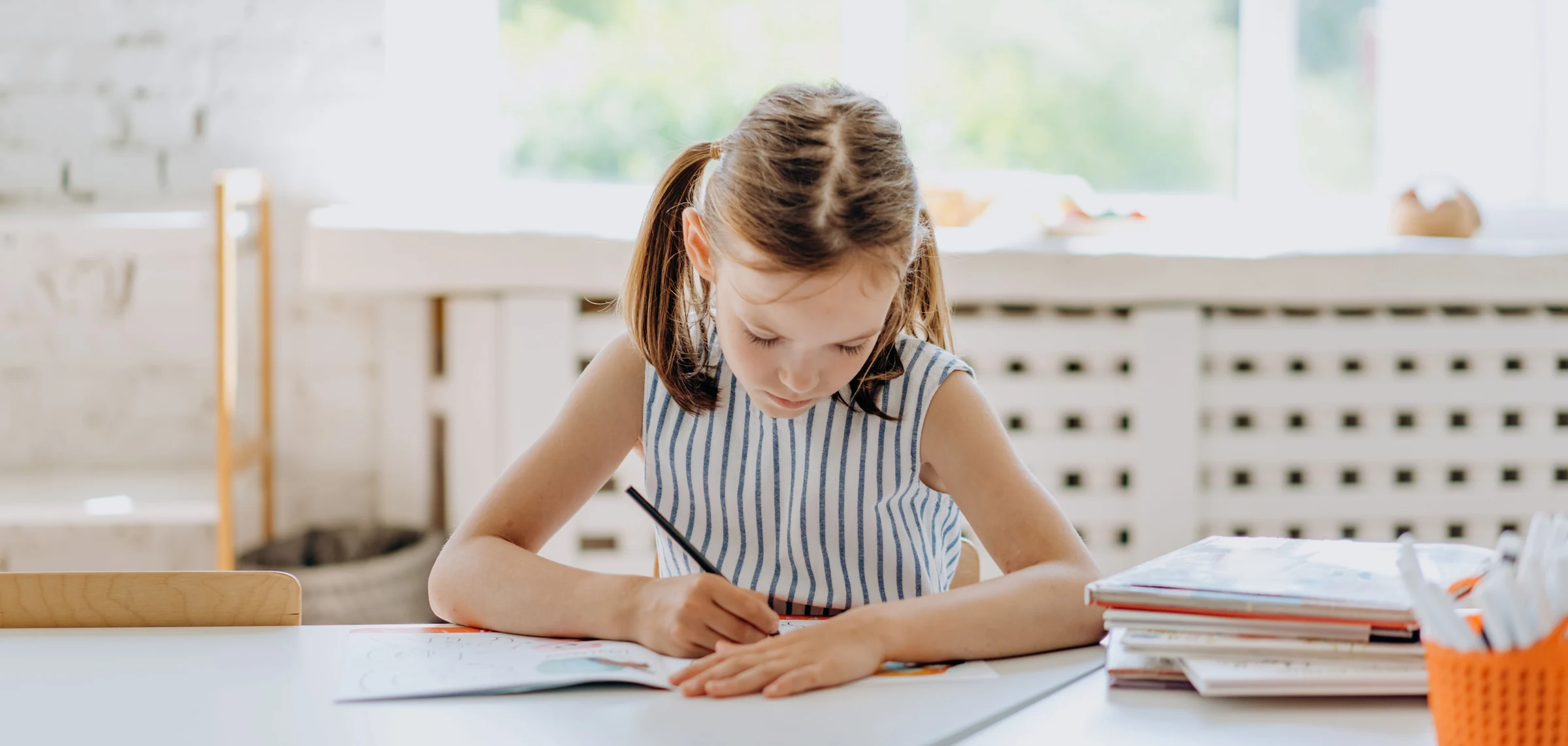 Leerling schrijft geconcentreerd aan een lichte tafel als beeld bij basisschoolbegeleiding.